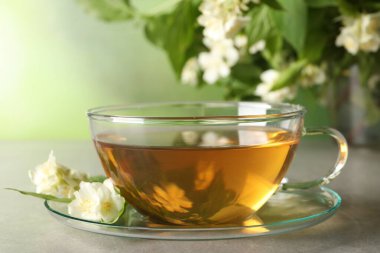 Aromatik yasemin çayı fincanda, çiçekler ve yeşil yapraklar açık gri masada