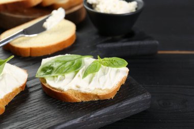 Krem peynirli ekmek parçaları ve siyah ahşap masada fesleğen. Metin için boşluk