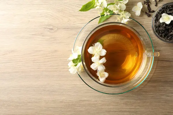 Aromatik yasemin çayı fincanda, çiçekler ve kuru yapraklar ahşap masada, üst manzara. Metin için boşluk