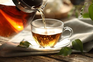 Pouring tea into cup on wooden table, closeup