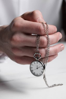 Man holding chain with elegant pocket watch at white table, closeup