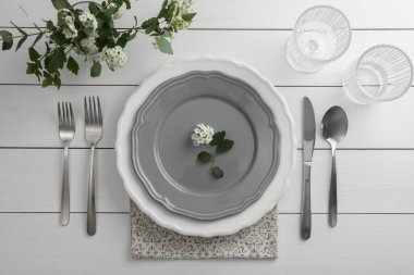 Beyaz ahşap masa üzerinde çatal bıçak, bardak ve tabaklar ile şık bir ortam.