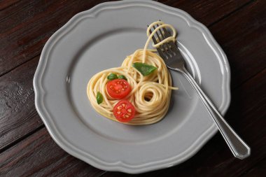 Tahta masadaki lezzetli spagetti, çatal, domates ve fesleğenden yapılmış kalp.