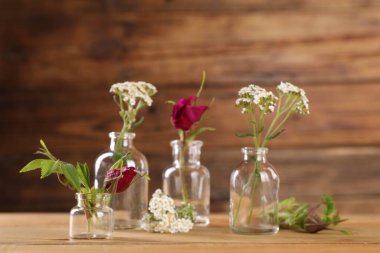 Different flowers in glass bottles on wooden table clipart