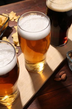 Bardaklar dolusu bira ve aperatifler ahşap masada, yakın plan.