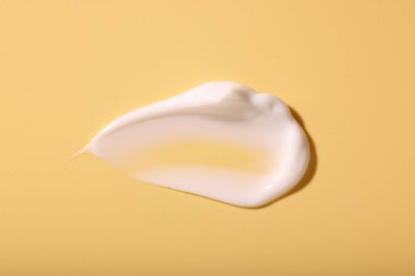 Soluk sarı arka planda yüz kremi örneği, üst görünümde.