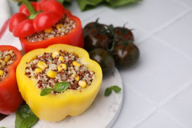 Quinoa dolgulu dolma biber, fesleğen ve domatesler beyaz fayanslı masada, yakın plan. Metin için boşluk