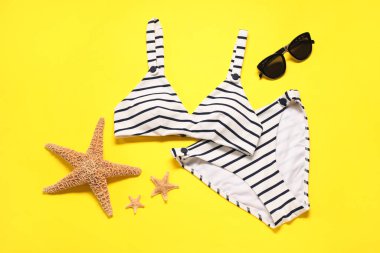 Sarı zemin üzerinde çizgili mayo ve güneş gözlüğü olan düz bir kompozisyon.