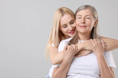 Family portrait of young woman and her mother on light grey background. Space for text
