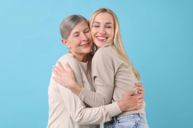 Family portrait of young woman and her mother on light blue background
