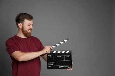 Making movie. Smiling man with clapperboard on grey background. Space for text