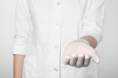Doktor açık gri arka planda bir şey tutuyor, yakın plan.
