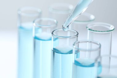 Işık arka planında pipetten test tüpüne sıvı damlatılıyor, yakın plan