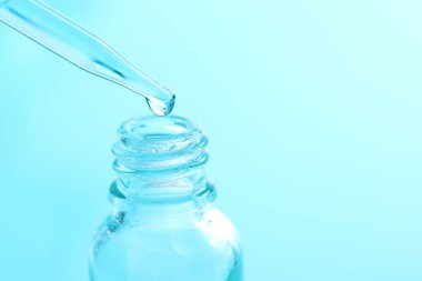 Açık mavi arka planda pipetten cam şişeye sıvı damlatıyor, yakın plan. Metin için boşluk