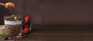 Tahta masada yoğurt ve tahıl gevreğiyle tatlıya bal dökmek. Metin için alanı olan pankart tasarımı