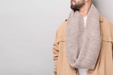 Açık gri arka planda, sıcak eşarplı, gülümseyen adam, yakın plan. Metin için boşluk