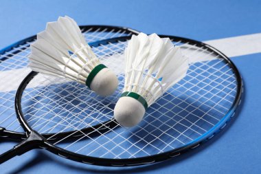 Tüylü badminton mekikleri ve raketleri mavi arka planda yakın plan