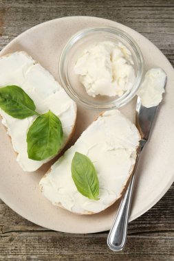 Krem peynirli lezzetli sandviçler ve ahşap masa üzerinde fesleğen yaprakları.