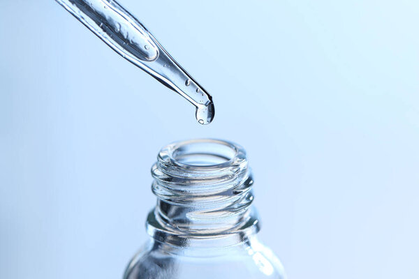 Dripping liquid from pipette into glass bottle on light blue background, closeup