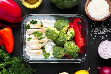 Sağlıklı yemek. Taze brokoli, tavuk, pirinç ve biber diğer ürünlerin yanında cam kabın içinde, siyah masada, düz yerde.