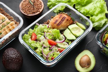 Sağlıklı yemek. Taze salata, avokado, pirzola ve karabuğday diğer ürünlerin yanında, siyah masada.