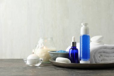 Spa kompozisyonu. Kozmetik ürünleri, terry havlusu, yanan mumlar ve deniz tuzu gri masada ışık arka planına karşı, metin için boşluk