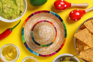 Meksika şapkası, tekila, nachos cipsi, guacamole ve maracas sarı arka planda, düz uzanma