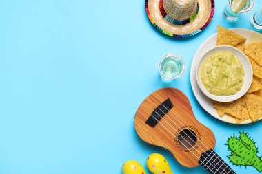 Meksika şapkası, ukulele, tekila, cips, avokado sosu ve açık mavi arka planda marakas. Metin için boşluk