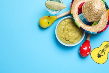Meksika şapkası, guacamole, marakas, tekila ve açık mavi arka planda kağıt gitar, düz yatak. Metin için boşluk