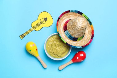 Meksika sombrero şapkası, guacamole, marakas ve açık mavi arka planda kağıt gitar.