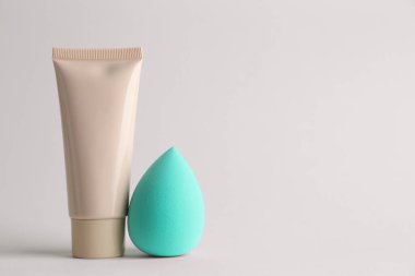 Açık gri arkaplanda makyaj süngeri ve cilt temeli, metin için boşluk