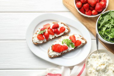 Çilekli lezzetli ricotta bruschetas ve roka beyaz ahşap masa, düz yatıyordu