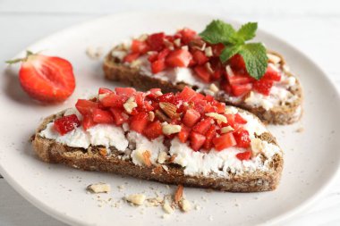 Ricotta peyniri, doğranmış çilek ve beyaz ahşap masada nane şekeri, yakın plan.