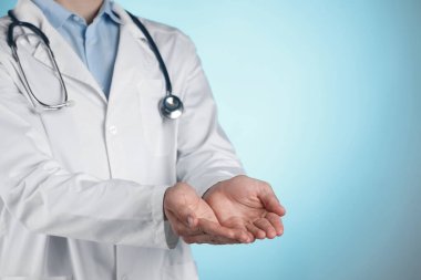 Doctor holding something on light blue background, closeup. Space for text