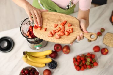Kadın mutfaktaki beyaz mermer masada blender ile nefis smoothie yapıyor.