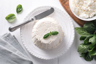 Taze ricotta (krem peynir) fesleğen ve bıçakla bembeyaz ahşap masa üzerinde, düz yatıyordu.