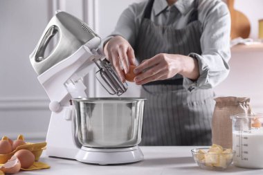 Kadın, kapalı bir masada hamur toplarken karıştırıcıya yumurta ekliyor, yakın plan.