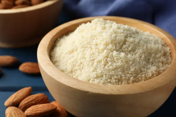 stock image Fresh almond flour in bowl and nuts on blue table, closeup