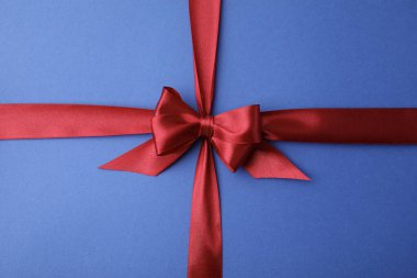 Mavi arka planda fiyonklu kırmızı saten kurdele, üst görünümde.