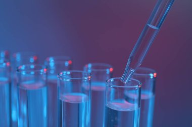 Renk arka planında pipetten test tüpüne sıvı damlatılıyor, yakın plan