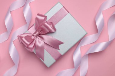 Pembe arka planda renk yaylı ve kurdeleli güzel hediye kutusu, düz yatıyordu.