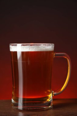 Mug with fresh beer on wooden table against color background