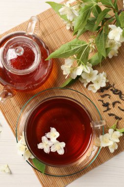 Sıcak yasemin çayı fincanda ve çiçekler beyaz ahşap masada, düz yerde.