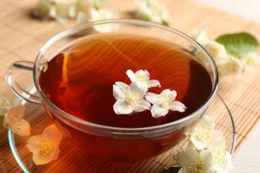 Sıcak yasemin çayı fincanda ve çiçekler beyaz ahşap masada, yakın plan