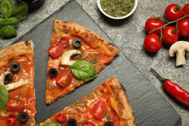 Fesleğenli lezzetli pizza, zeytin ve malzemeler gri desenli masada, düz yerde.