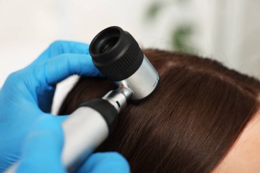 Dermatoskoplu trikoloğum klinikte hastanın saçını inceliyor.