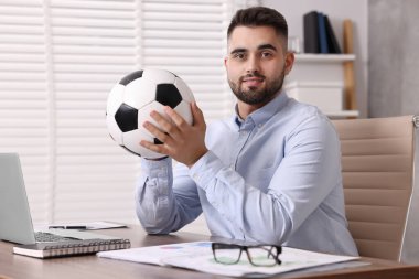 Masasında futbol topu olan genç bir adam.