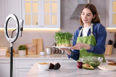 Yemek blogcusu mutfakta akıllı telefon ve yüzük lambasıyla video kaydederken yemek pişiriyor.