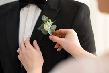 Gelin, damadın ceketine yaka çiçeği koyuyor, yakın plan. Düğün aksesuarı
