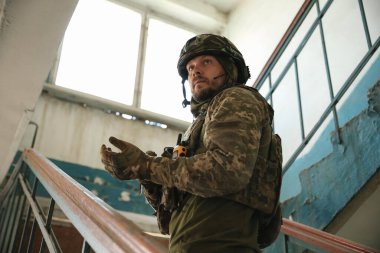 Military mission. Soldier in uniform on stairs inside abandoned building, low angle view